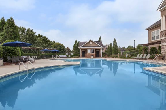 A large swimming pool in front of a house with a patio and umbrellas.at Carrington Place at Wildewood, Columbia, SC