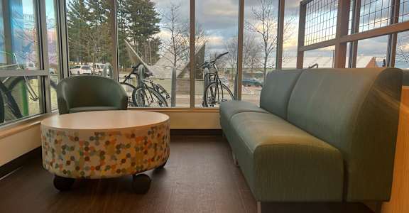 A round table with a patterned top sits in front of a window with a view of a bicycle and trees outside.