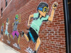 a mural on a brick wall of a boy running with a baseball glove in his hand