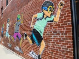 a mural on a brick wall of a boy running with a baseball glove in his hand