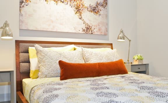 a bedroom with a bed with an orange pillow and a painting on the wall