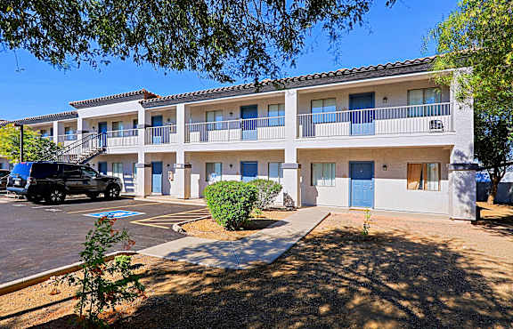A sunny day at a multi-story apartment complex with a parking lot in front.