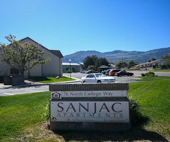 a sign apartments in front of a lawn with a car