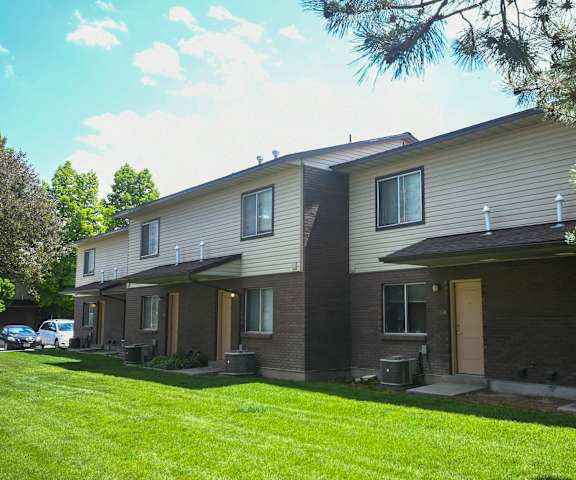 a white and brown apartment building with a lawn and trees