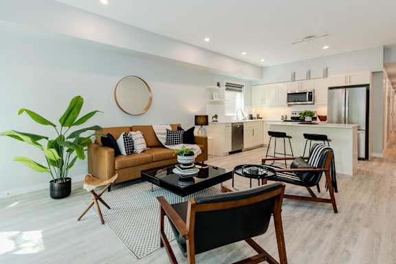 A modern living room with a brown sofa, a glass table, and a round mirror on the wall.