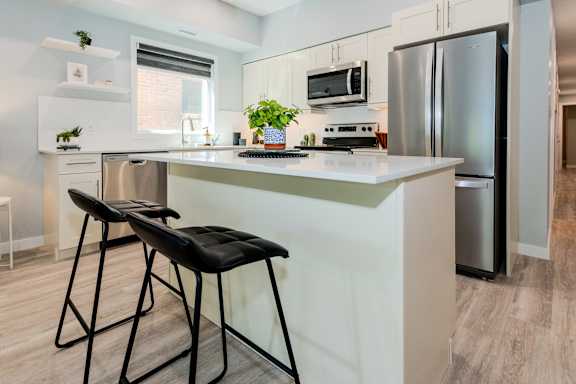 A kitchen with a white counter and two black barstools.