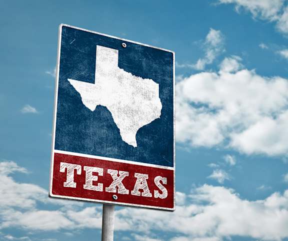 A Texas state sign against a blue sky with clouds.