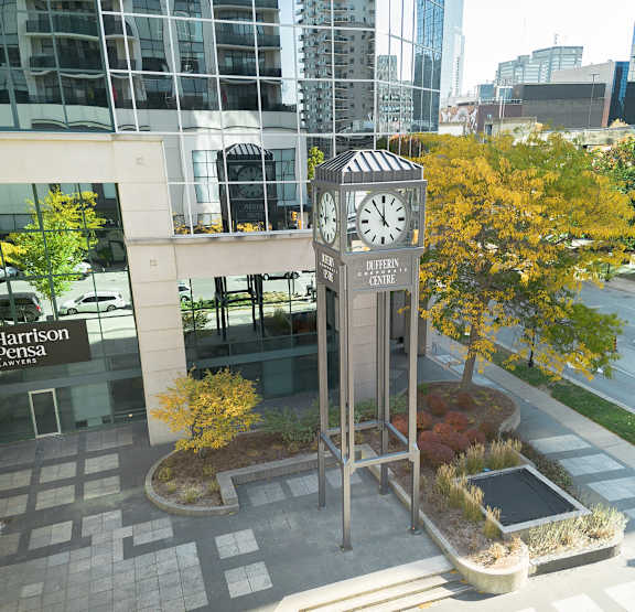 A clock tower in the middle of a courtyard with a building in the background.