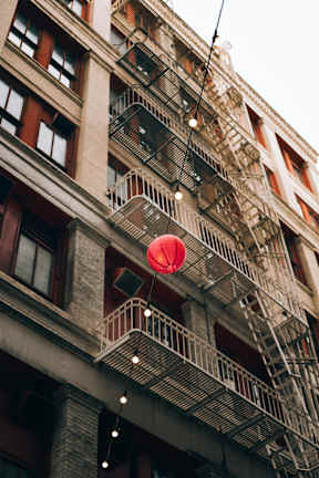 A red lantern hanging from a wire in front of a building with fire escapes.