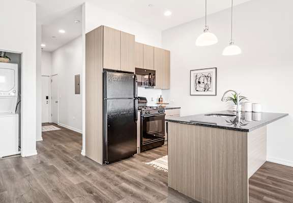 A modern kitchen with a black fridge and wooden cabinets.