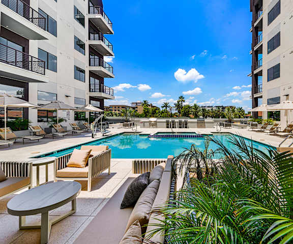 A pool surrounded by chairs and plants with apartment buildings in the background.