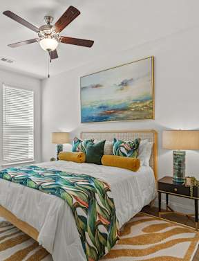 A bedroom with a bed, a ceiling fan, and a painting on the wall.