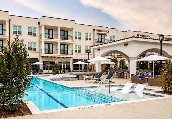 a swimming pool with lounge chairs and umbrellas in front of a building