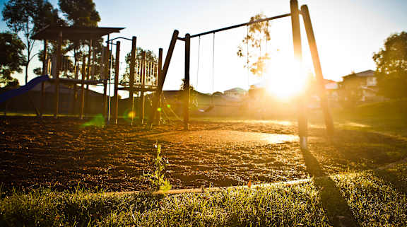 A playground with swings and a slide is bathed in sunlight at Pleasantview Apartments, Baltimore, Maryland