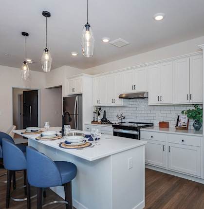 a kitchen with white cabinets and a white island with blue chairs