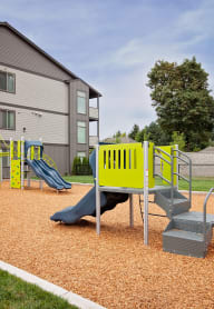 a playground with a slide and chairs in front of a building