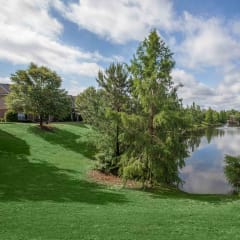 A serene landscape with a pond, trees, and a house in the background.at Carrington Place at Wildewood, Columbia, SC 29223