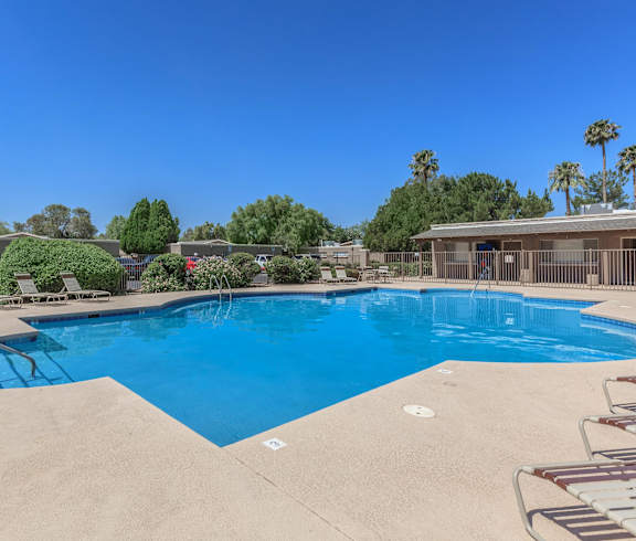 A large swimming pool surrounded by a concrete patio and lounge chairs.