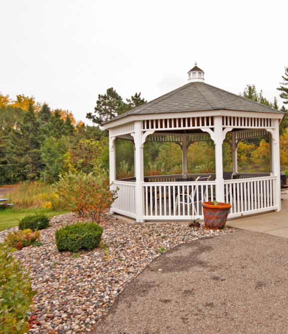 A gazebo is surrounded by a gravel area and a small garden.