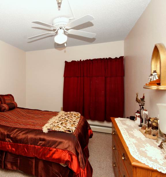 A bedroom with a bed, dresser, and ceiling fan.
