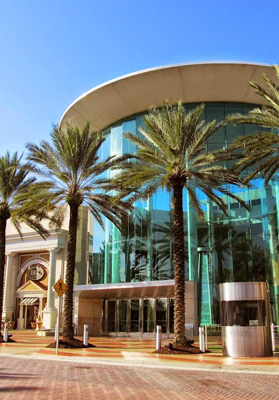 A modern building with a curved glass facade and palm trees in front.