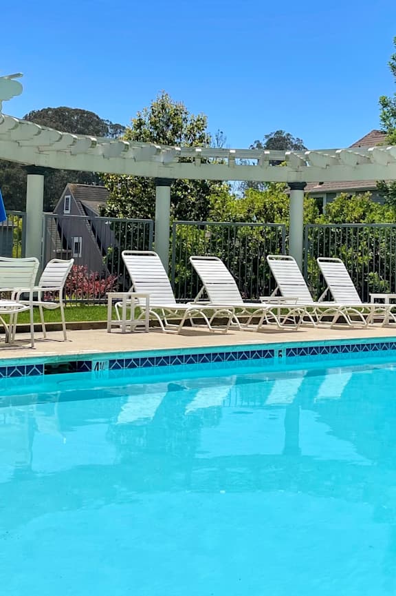 A pool with a white pergola and blue umbrellas. at Westmont Place Townhomes Apartments, Santa Cruz, 95060