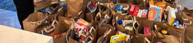 two women standing next to a pile of bags of food