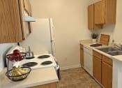 Thumbnail 6 of 17 - Bridgeside Landing Apartments in Taylorsville, Utah, Kitchen with wood cabinets, stove, fridge, dishwasher and double sink.