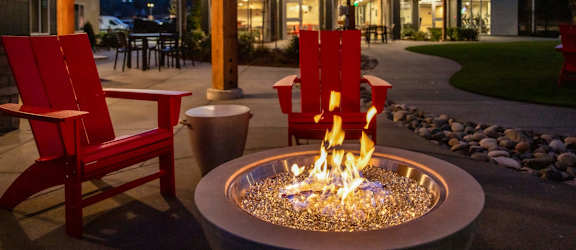a fire pit with red chairs and a building in the background