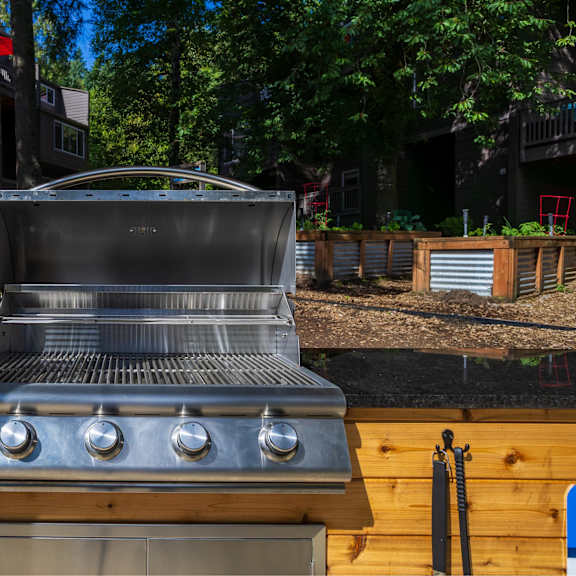 A ULZAZ grill is on a wooden deck with trees in the background.