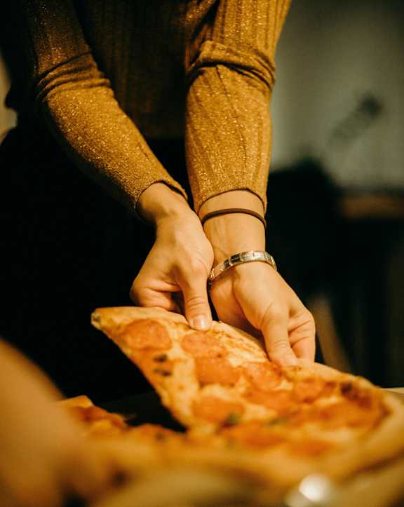 A person in a brown sweater is cutting a pizza.