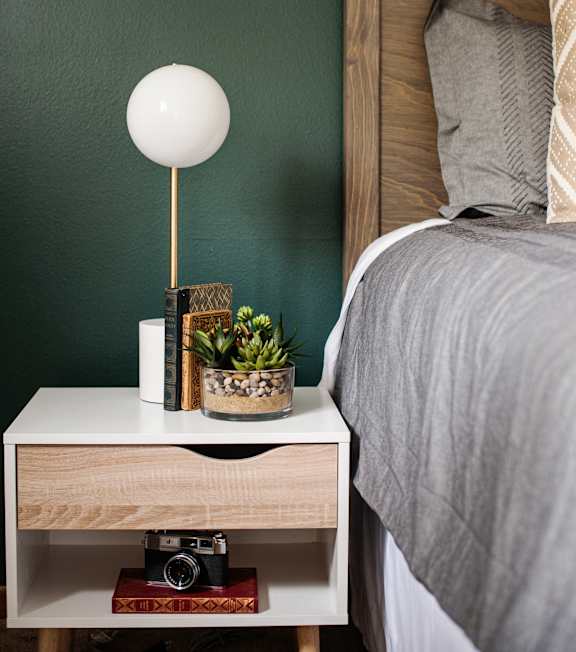 a bedroom with a bed and a nightstand with a lamp and a plant