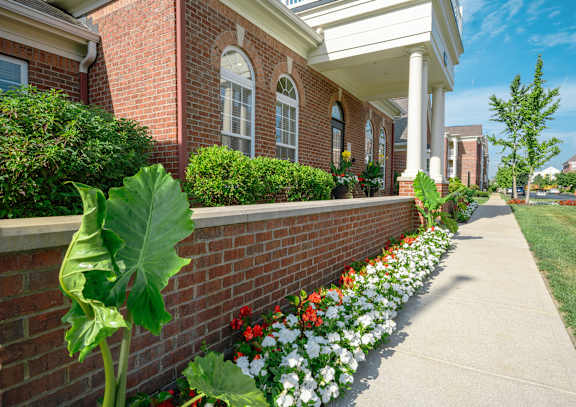 A brick building with a white porch and a flower bed in front at Alexandria of Carmel Apartments, Carmel, Indiana