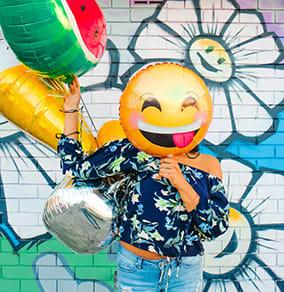 Happy woman taking a photo in front of graffiti wall with balloons.