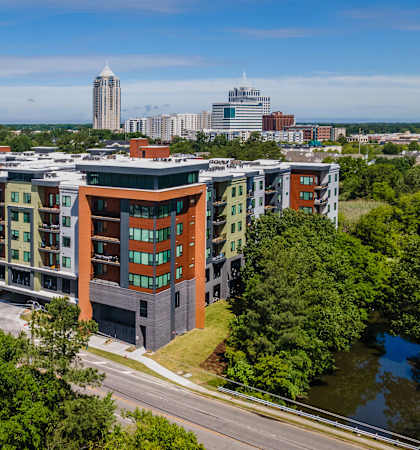 A large apartment complex is surrounded by trees and is located near a highway.