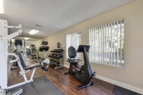 Community Fitness Center with Excercise Bike, Handweights, Treadmills, Ellipticals, Weight Machine, Plastic Floor Mats, Open Blinded Windows, Full Mirror and Wood Inspired Floor