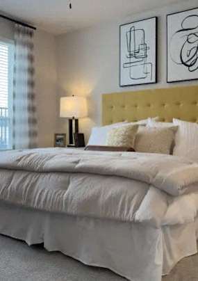A bed with white sheets and pillows sits in a room with two framed artworks on the wall.