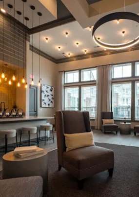 A brown chair with a white pillow is in the middle of a room with a bar and a window.