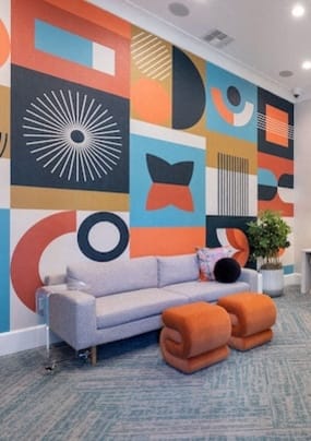 a living room with a couch and chairs and a wall with a mural