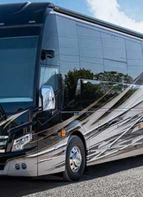 A black and silver bus is parked on a gravel lot.