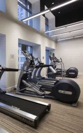A treadmill is in the foreground of a well-lit gym with various exercise equipment.