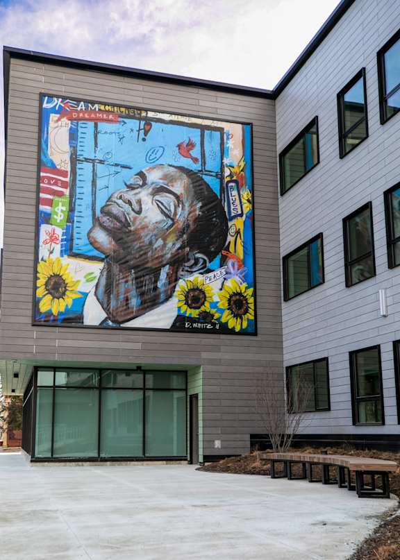 A mural of a man's face with sunflowers and a flag is painted on the side of a building.