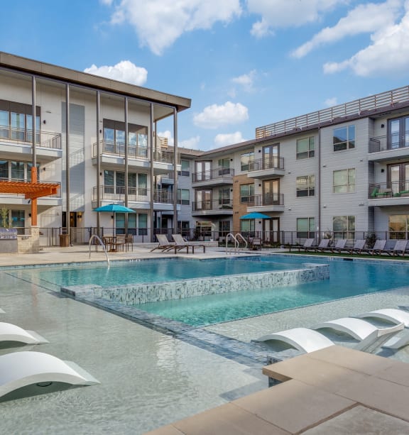 a resort style pool with lounge chairs and umbrellas in front of a building