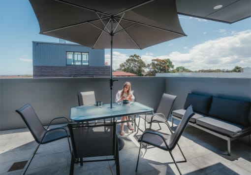 a woman sitting at a table under an umbrella on a patio