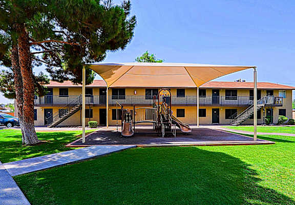 A playground area with a slide and a swing set in front of a building with a yellow awning.