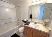 Thumbnail 7 of 17 - Bridgeside Landing Apartments in Taylorsville, Utah, Bathroom with bathtub and shower, round white sink, wooden cabinets under the sink.