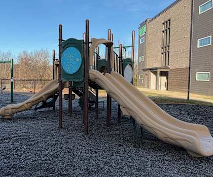 A playground with a slide and a green sign with a blue circle and a white symbol in the middle.