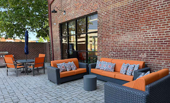 A patio with a black wicker couch and orange cushions.