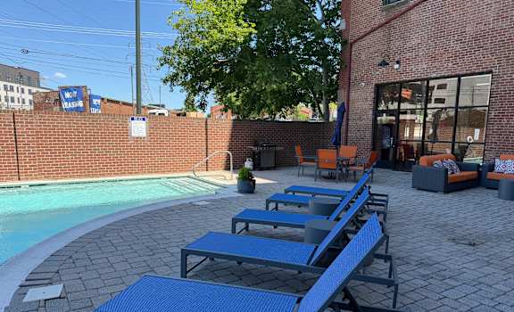 A poolside area with blue sun loungers and a brick building in the background.