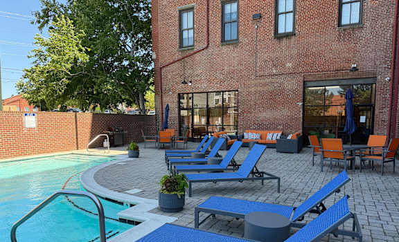 A pool with blue loungers and a brick building in the background.